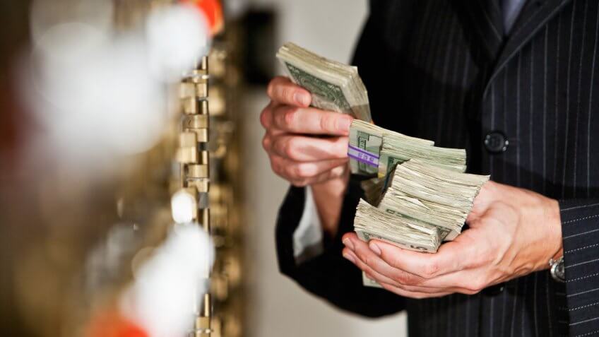 Man holding big stack of US paper currency by safety deposit boxes.
