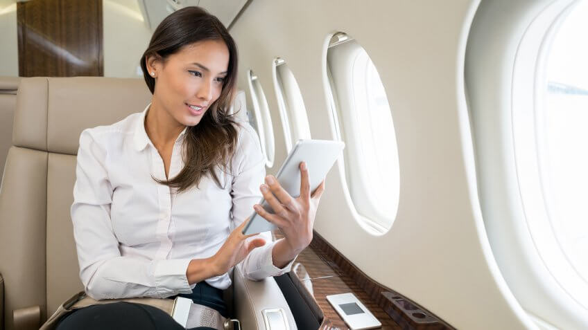 Business woman traveling and enjoying onboard entertainment on her tablet computer.