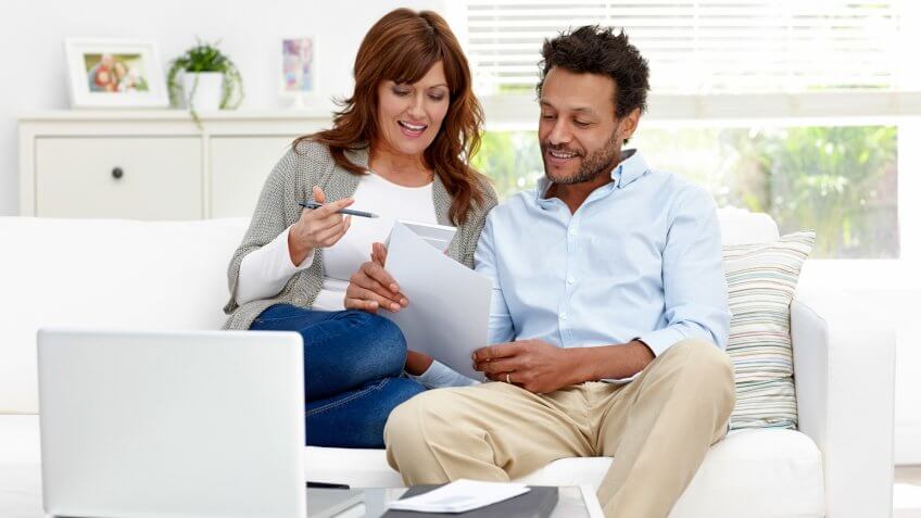 Portrait of interracial couple sitting together on sofa calculating monthly expenses - The pictures on the dresser or window or side board belong to the photographer.