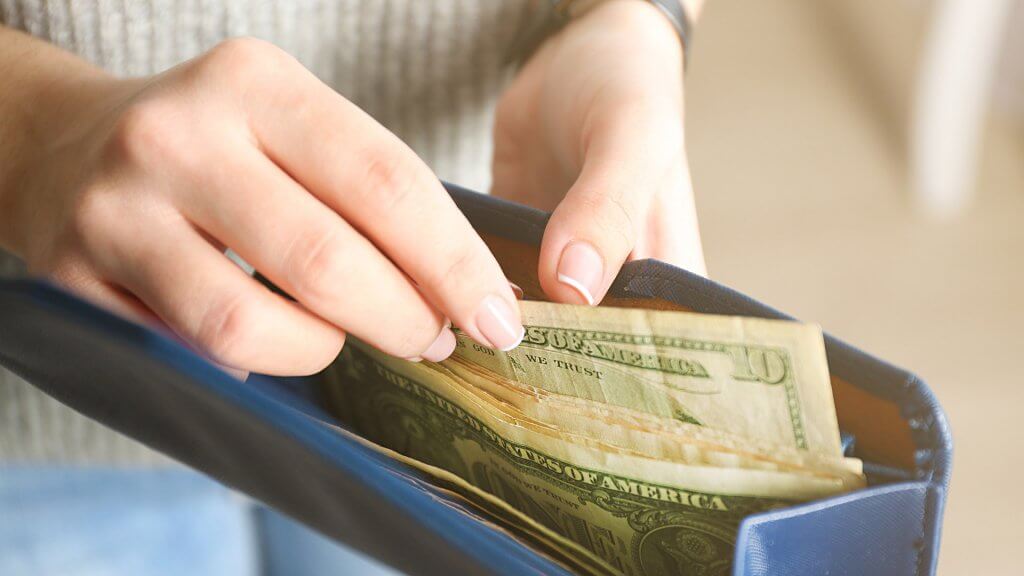 Rein In Your Spending Now woman removing cash from purse