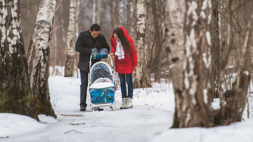 mother and father pushing baby in stroller through the woods