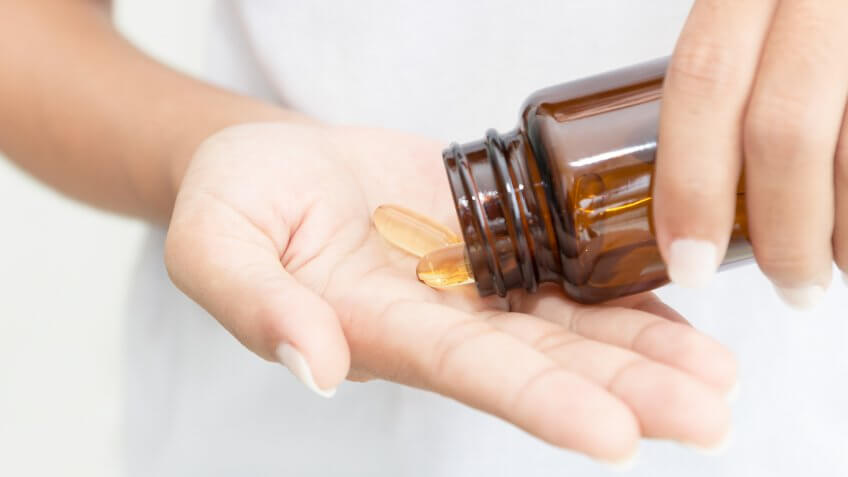 person pouring health supplements into hand from pill bottle