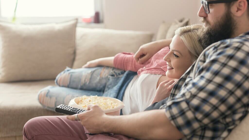 Make Staying In the Main Event couple eating popcorn and watching tv on the couch together