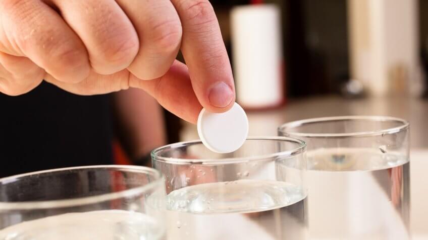 Person dropping an alka seltzer into glass of water