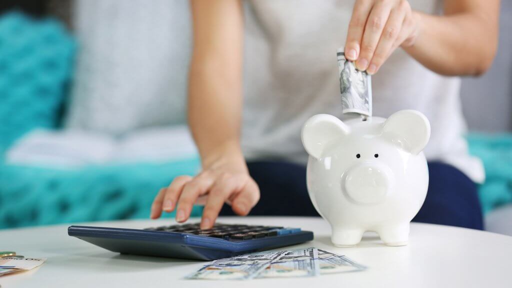 Turn Saving Into a Game woman inserting 100 dollar bill into piggy bank