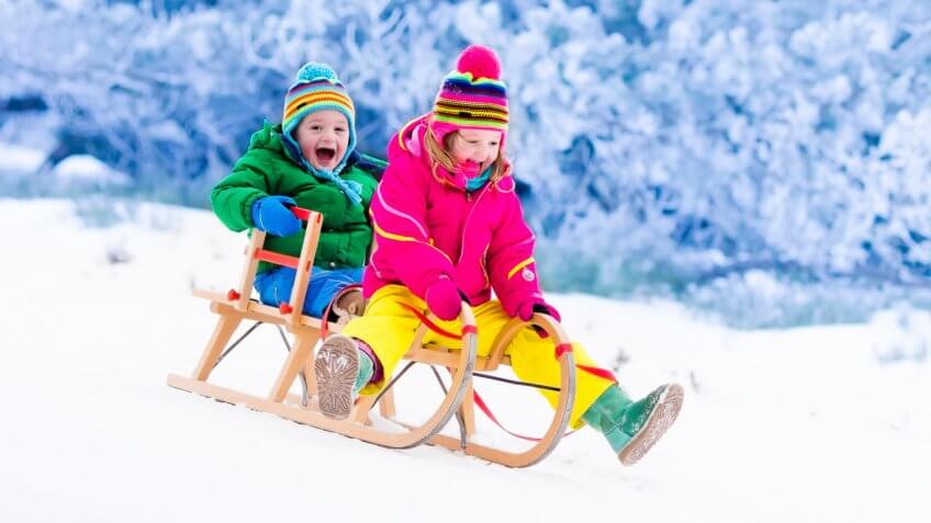 little boy and girl riding down hill on sled together
