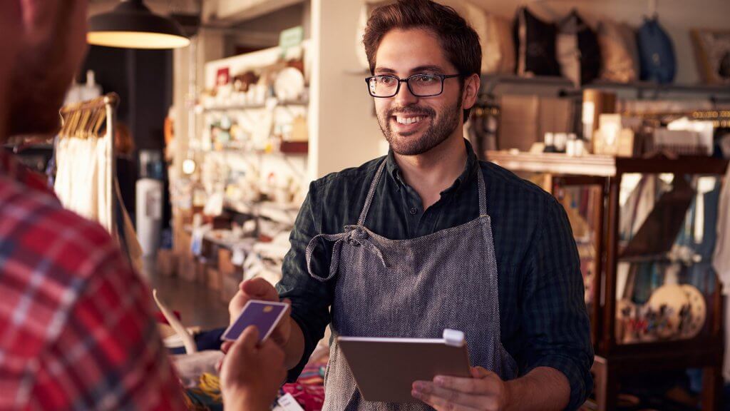Ask for a Lower Price male employee in apron receiving credit card from customer