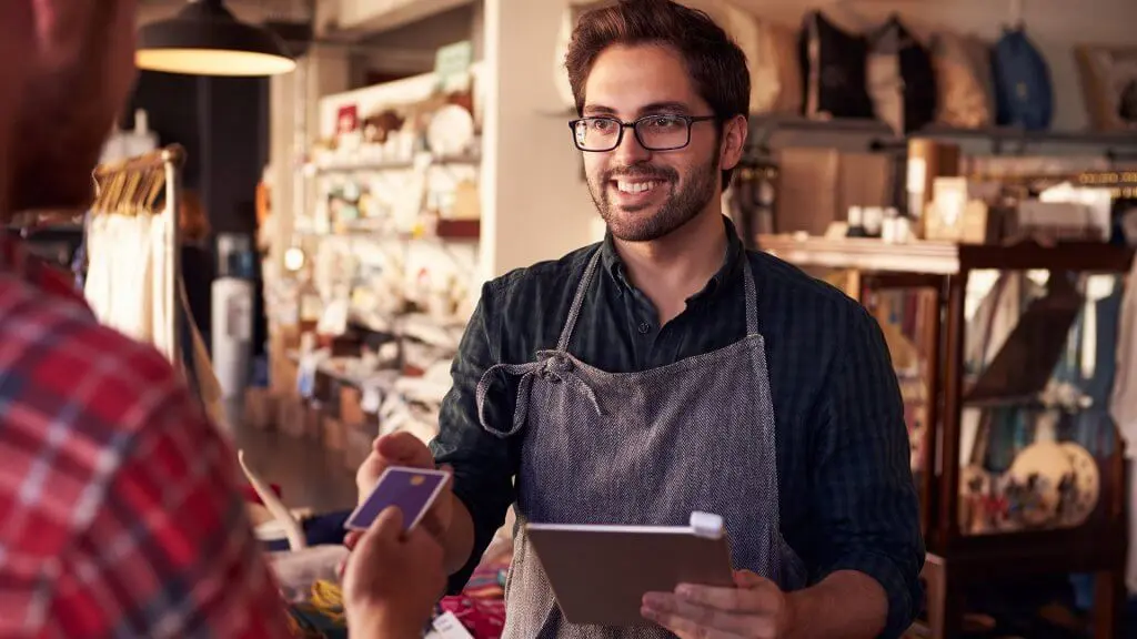 male employee in apron receiving credit card from customer