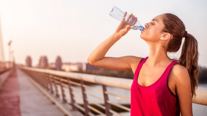 woman in workout attire drinking a plastic bottle of water