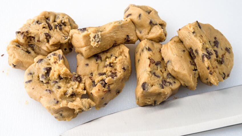 Several chunks of chocolate chip cookie dough on a plastic cutting board with a knife.