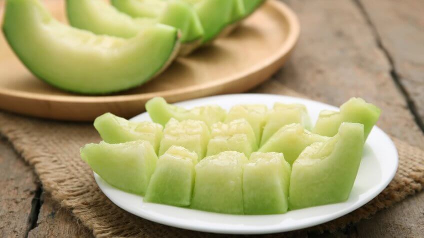 Green cantaloupe melon slices on wooden table.