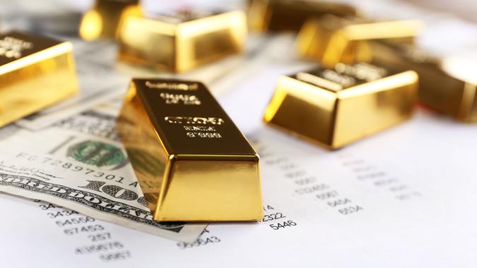 gold blocks on top of hundred dollar bills and data spreadsheet