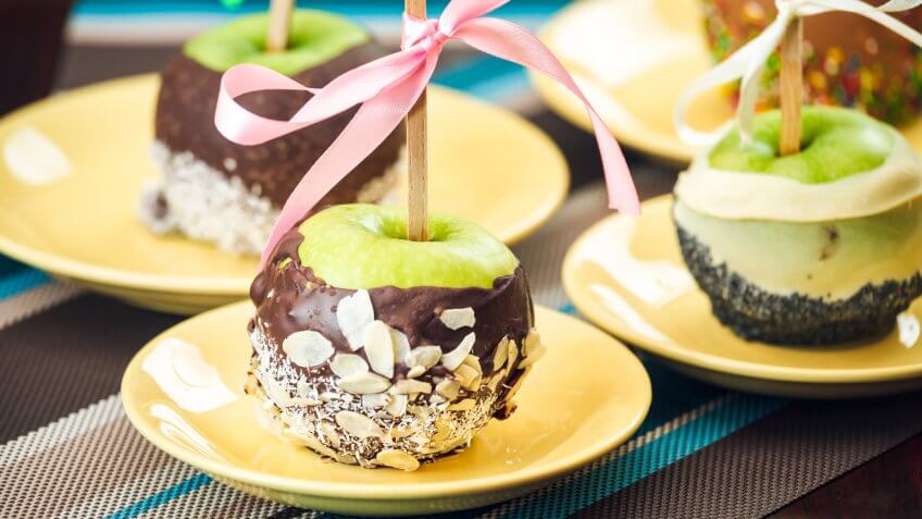 Group of Chocolate coated green apples on plates.