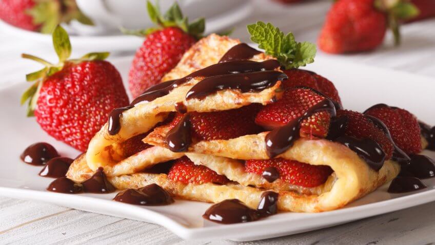 Delicious crepes with fresh strawberries and chocolate close-up on a plate.