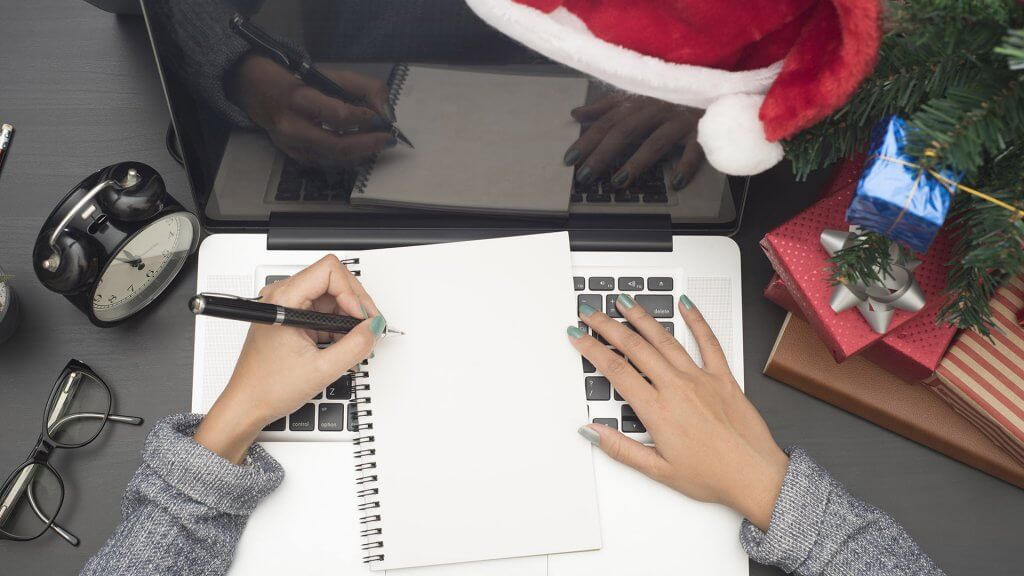 Create a Plan and Get Organized overhead shot of womans hands taking notes near christmas tree