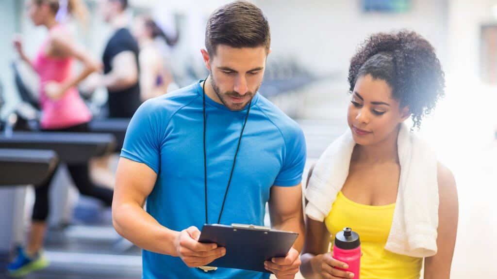 Choose an Active Job personal trainer looking at clipboard with woman