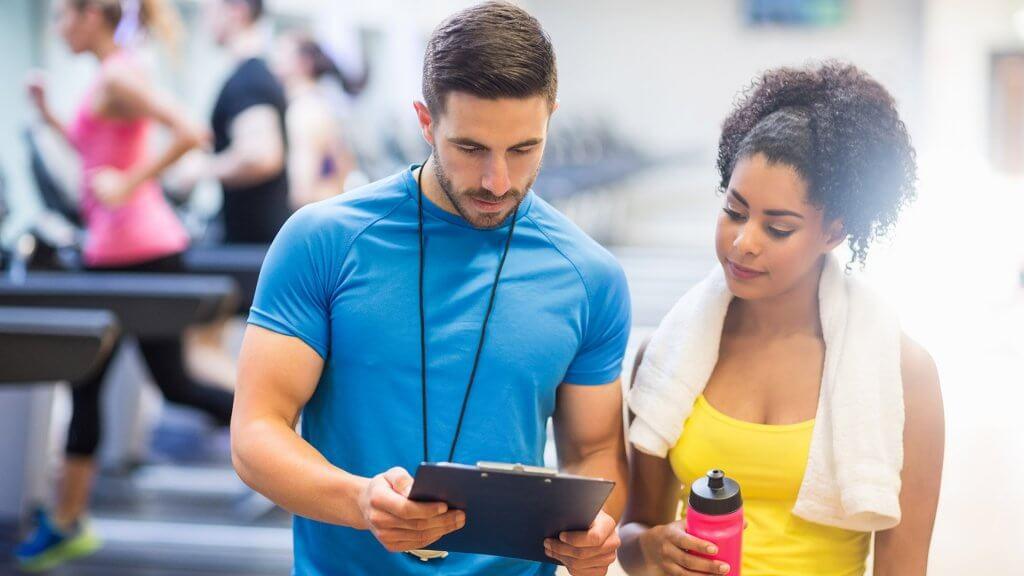 personal trainer looking at clipboard with woman