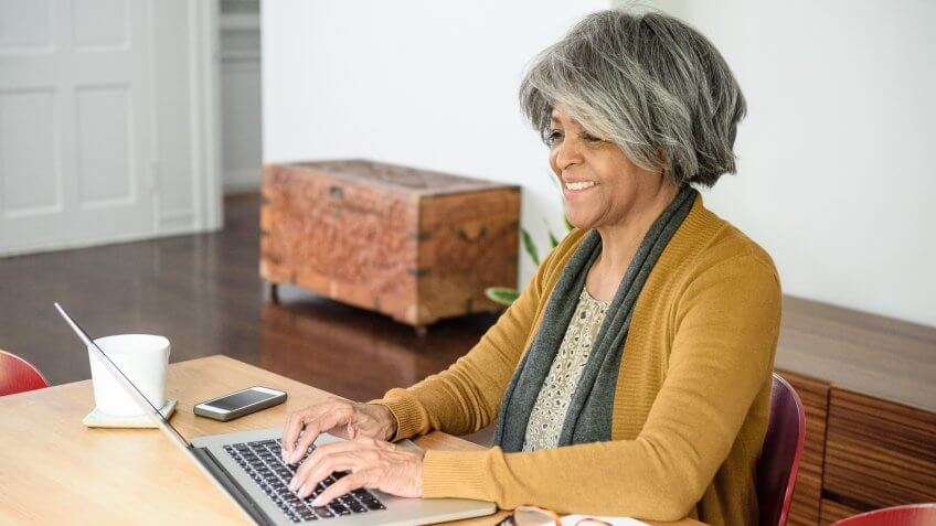 Surfing the web at home, sitting at table typing on laptop keyboard.