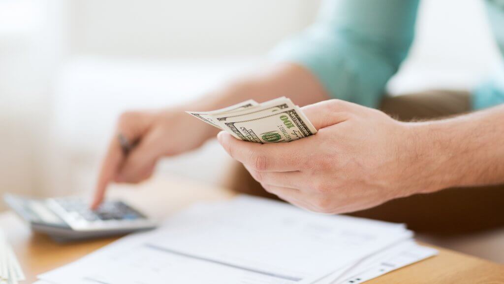 Automating Savings Is Less Painful woman holding cash and using calculator