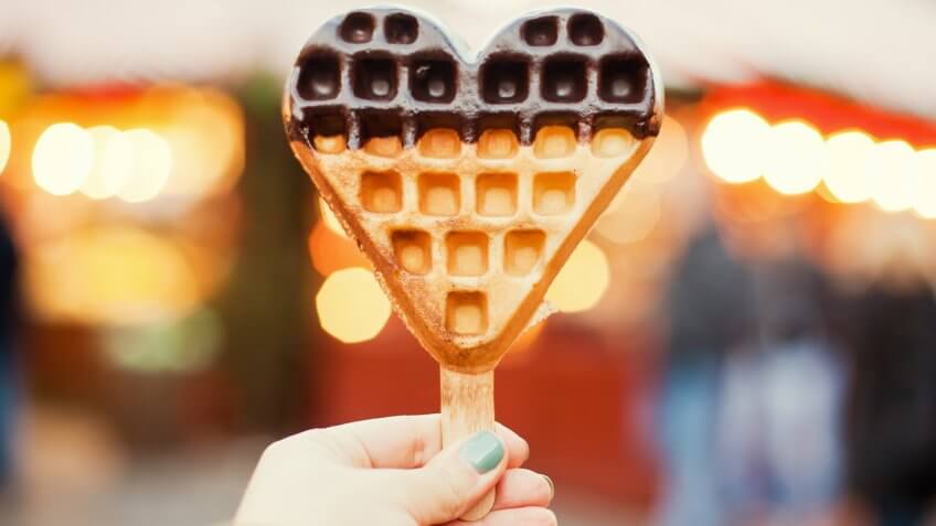 Heart-shaped freshly baked waffle in the hand.
