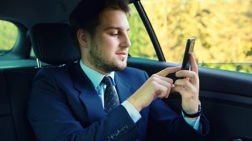 man in the back of a car on his cell phone
