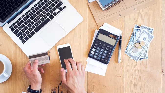 Hands holding credit card and paying bills on table.