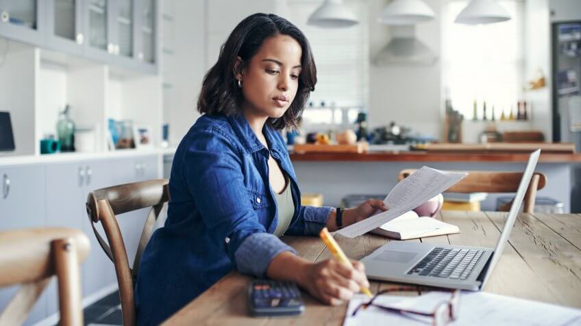 Shot of a young woman using a laptop and going through paperwork while working from home.