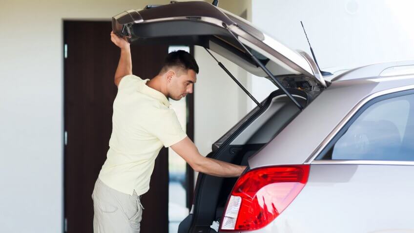 road trip, transport, private property leisure and people concept - young man with open car trunk at parking space.