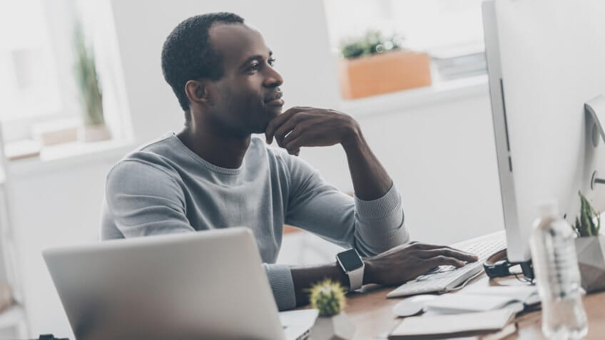 Handsome young African man keeping hand to his face while sitting at his working place in home office.