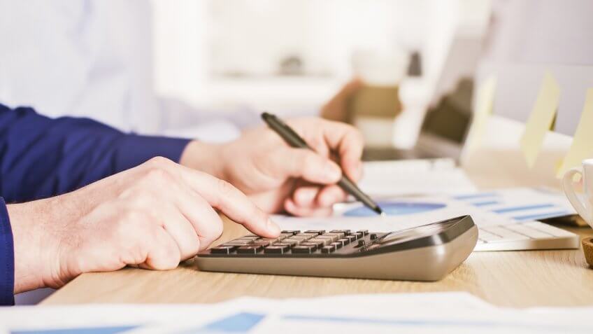 person using calculator and writing on a paper with charts and graphs on it
