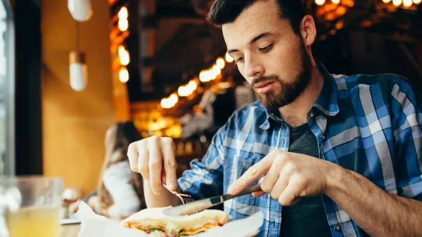 man cutting his sandwich with a fork and knife