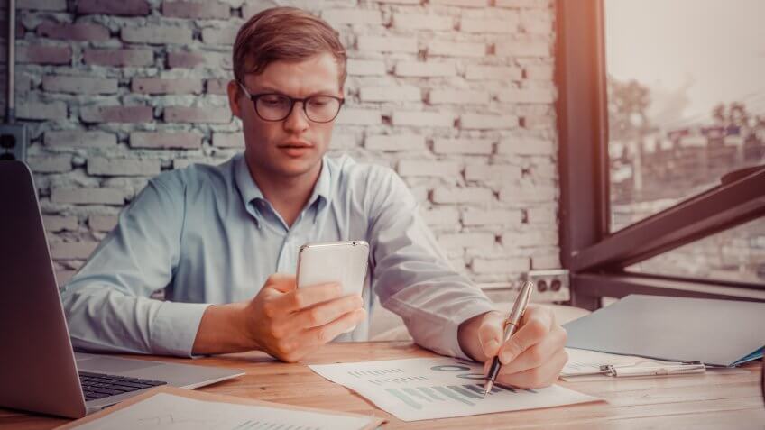 Young business man sitting in office at table and using smartphone.