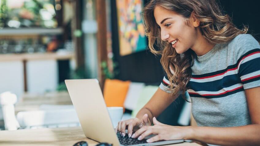 Attractive young woman sitting in cafe and typing on a laptop, with copy space.