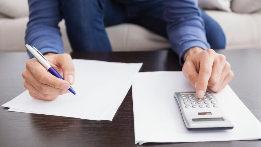 man writing on a paper whilst typing into a calculator