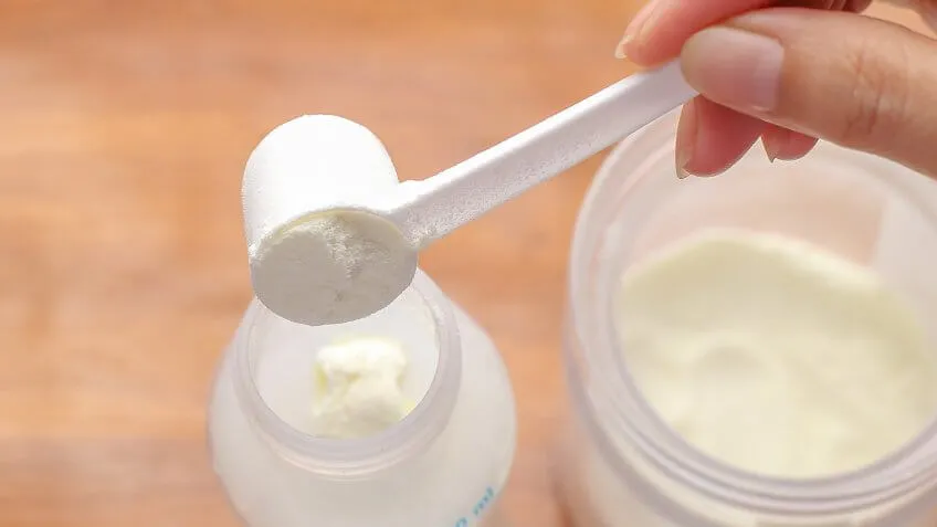 woman scooping infant formula into a baby bottle