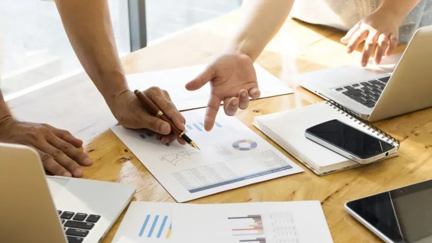 two people pointing at charts and graphs around laptop and tech