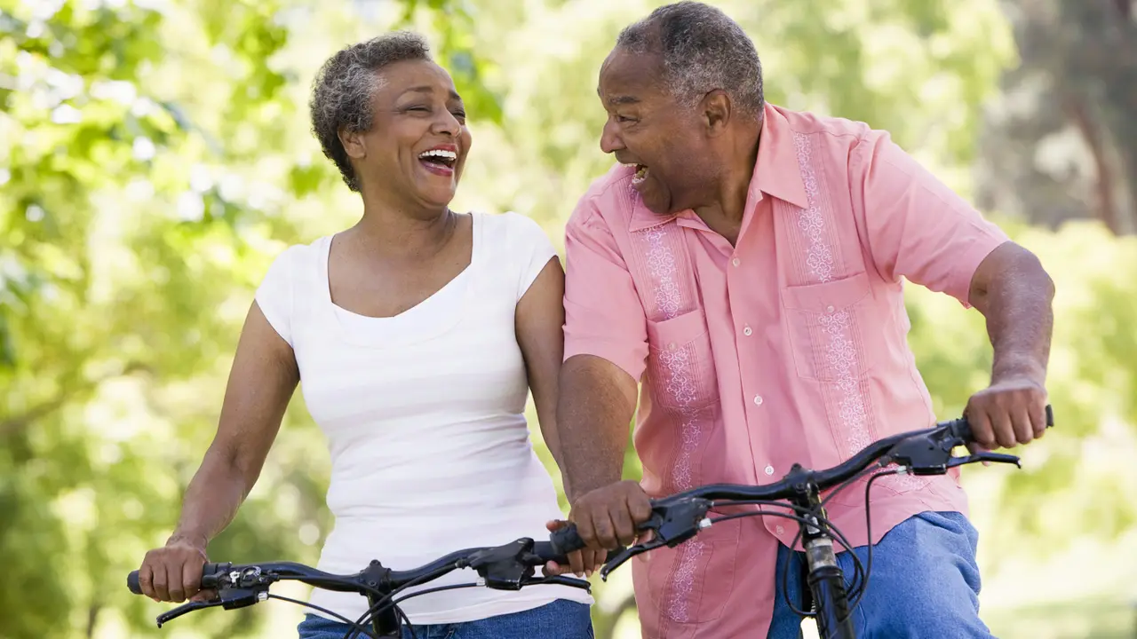 Happy senior or retired couple riding bicycles through woods or neighborhood to show retirement comfort.