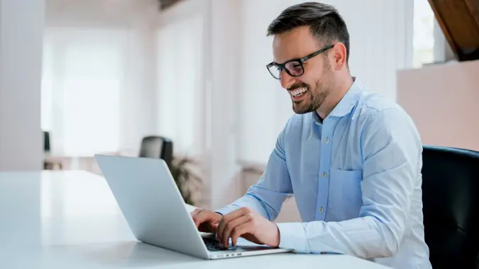 A man smiles as he works on his laptop at home.