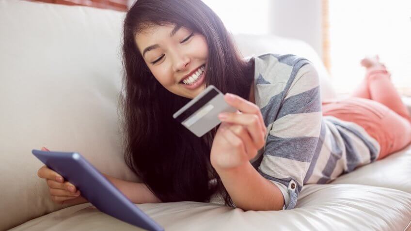 happy woman looking at her credit card holing a smart tablet ipad