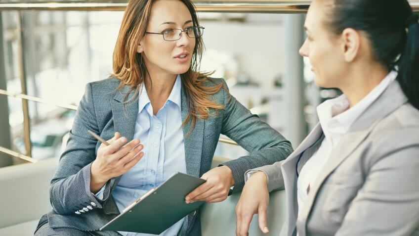 two women in suits speaking to each other, one holding a clipboard