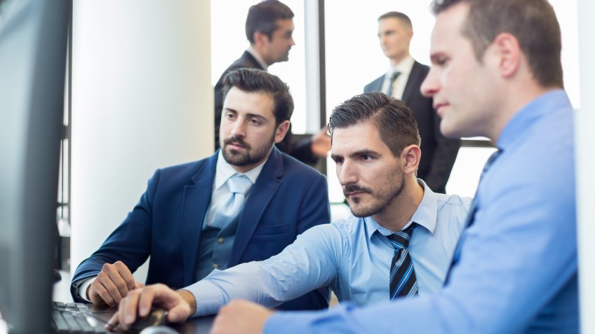 group of men sitting around a computer