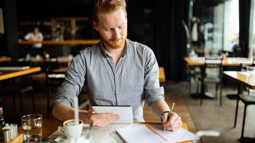 man writing in his notebook working at a coffee shop