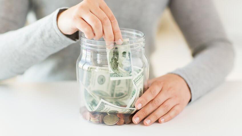woman placing $100 in a glass jar