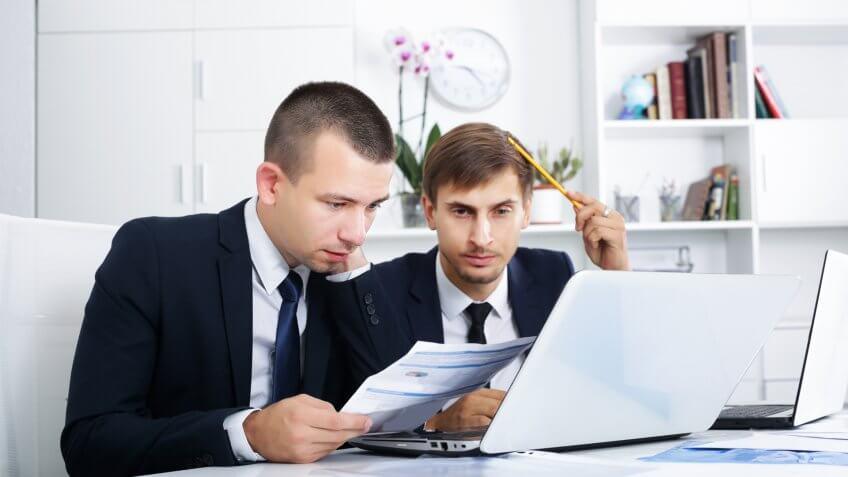two young confused business men staring at documents and laptop
