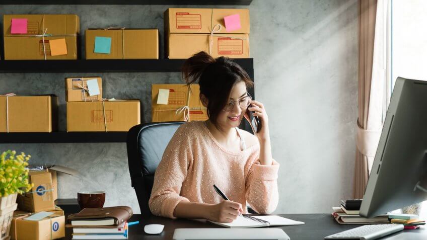 woman on the phone writing in a notebook in her work space