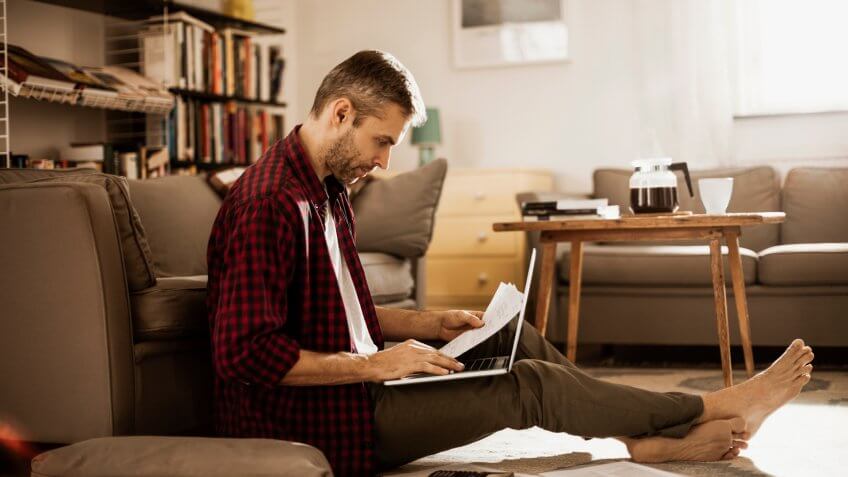 Photo of a man sitting on the floor and working on laptop.