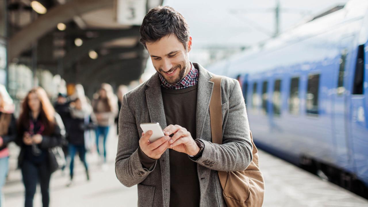 Photo of a smiling businessman texting on his mobile phone at train station.