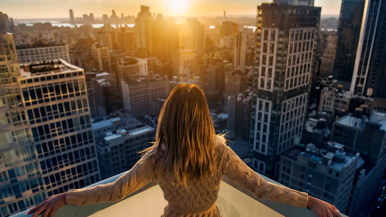 Rich woman enjoying the sunset standing on the balcony at luxury apartments in New York City.