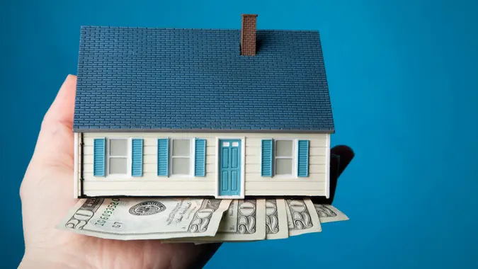 hand holding cash and a small house