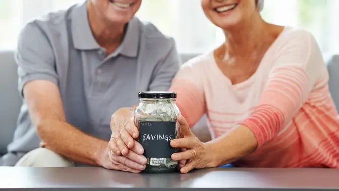 Shot of a senior couple proudly posing with their savings jar.